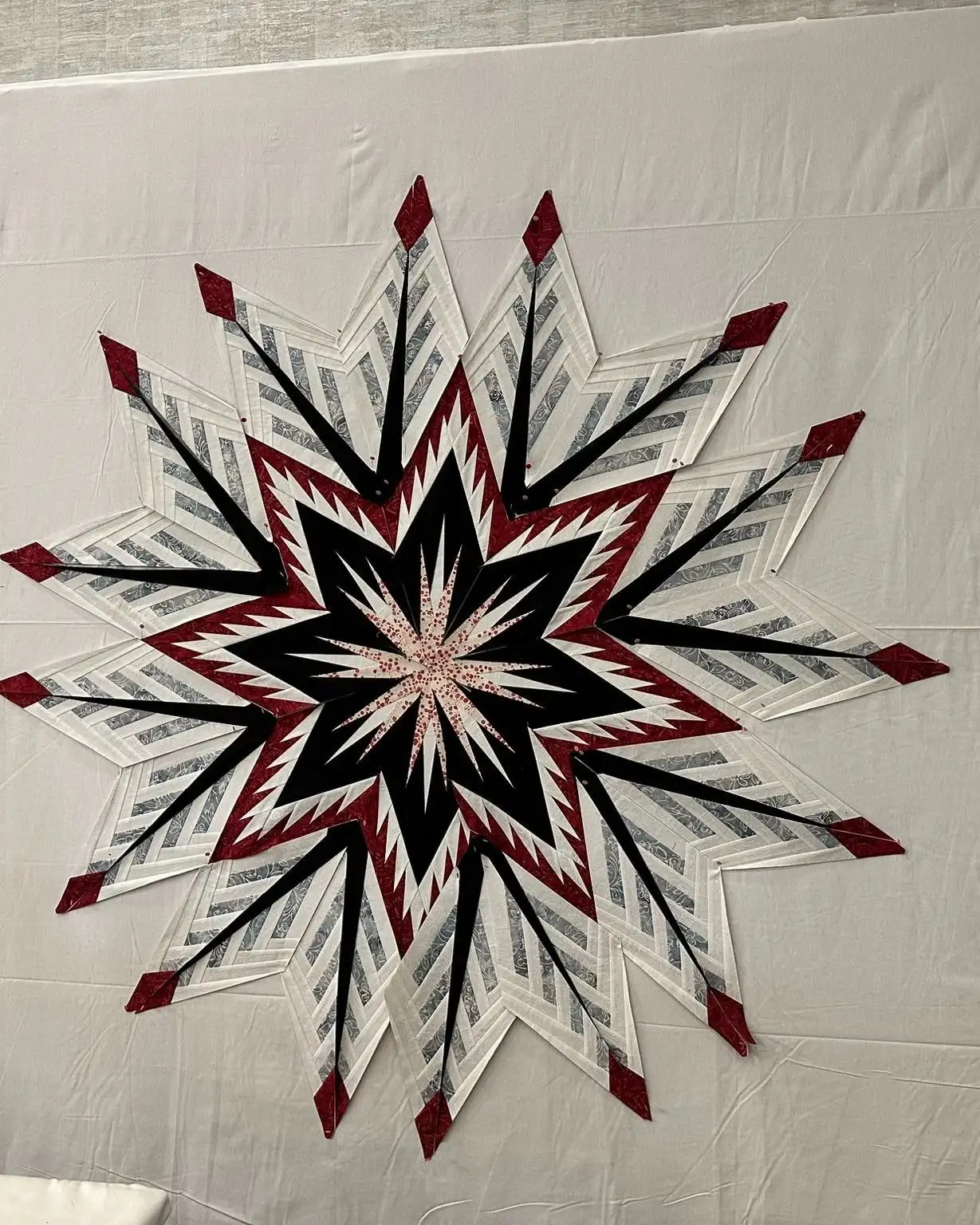 A finished Judy Niemeyer star quilt in red, black and white hanging on a wall
