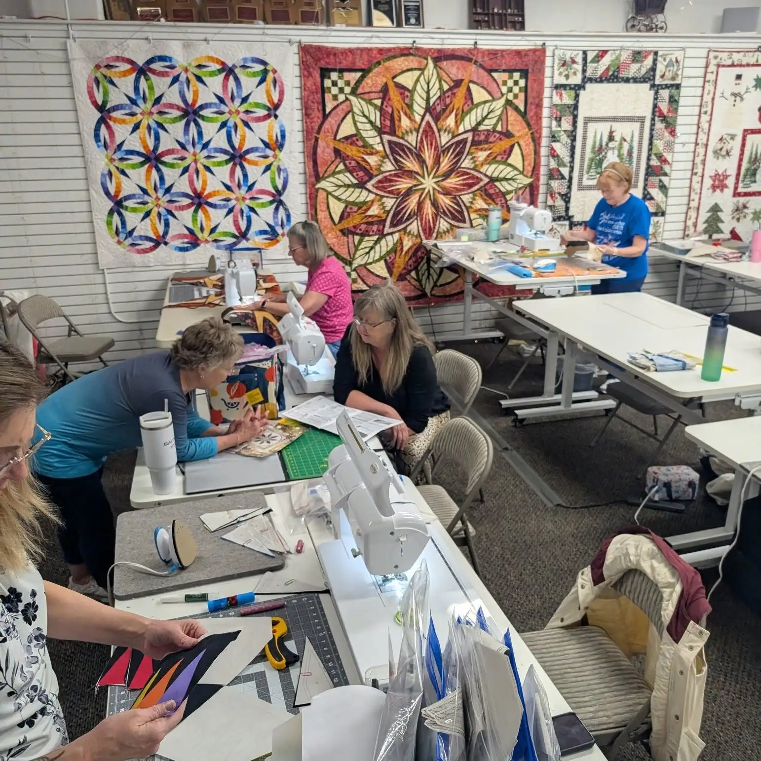 Quilters cutting fabric for a Quiltworx class, with finished Judy Niemeyer quilts on the wall